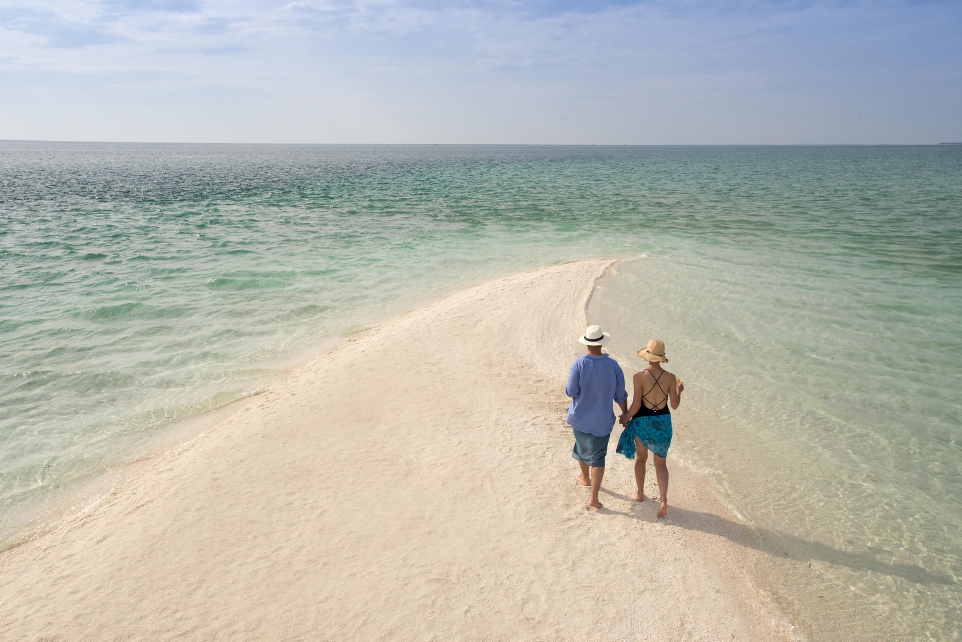 Couple walking along a white sandbar into the Indian Ocean