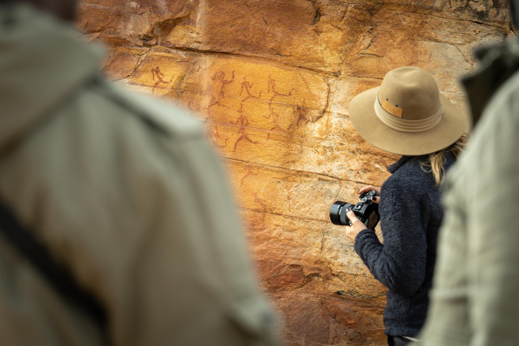 Traveler photographing ancient San rock art paintings on a golden sandstone wall