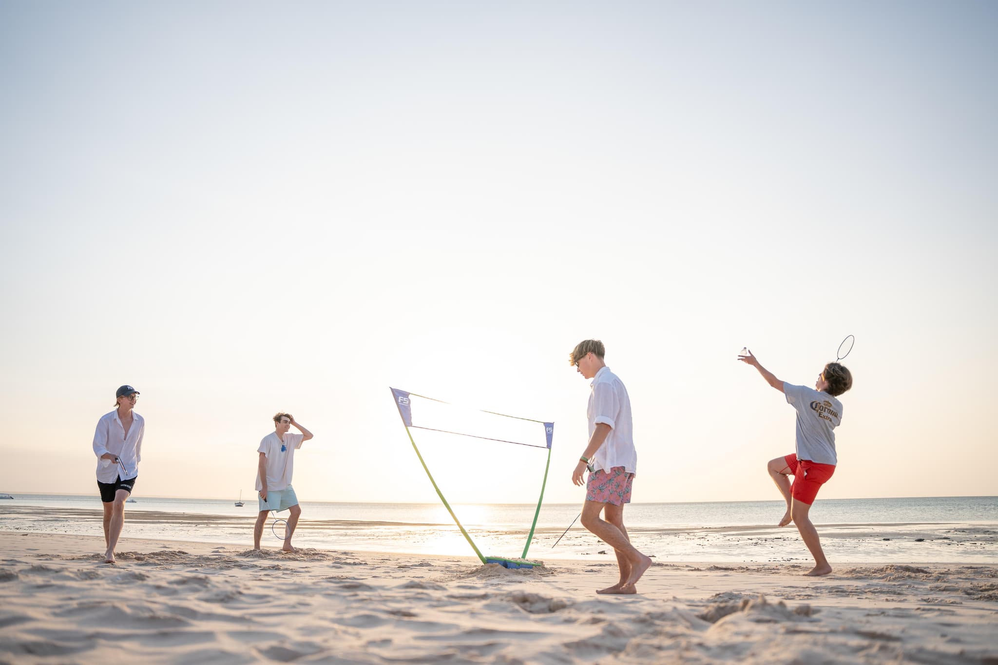 Teenagers playing beach badminton on pristine sand at sunset