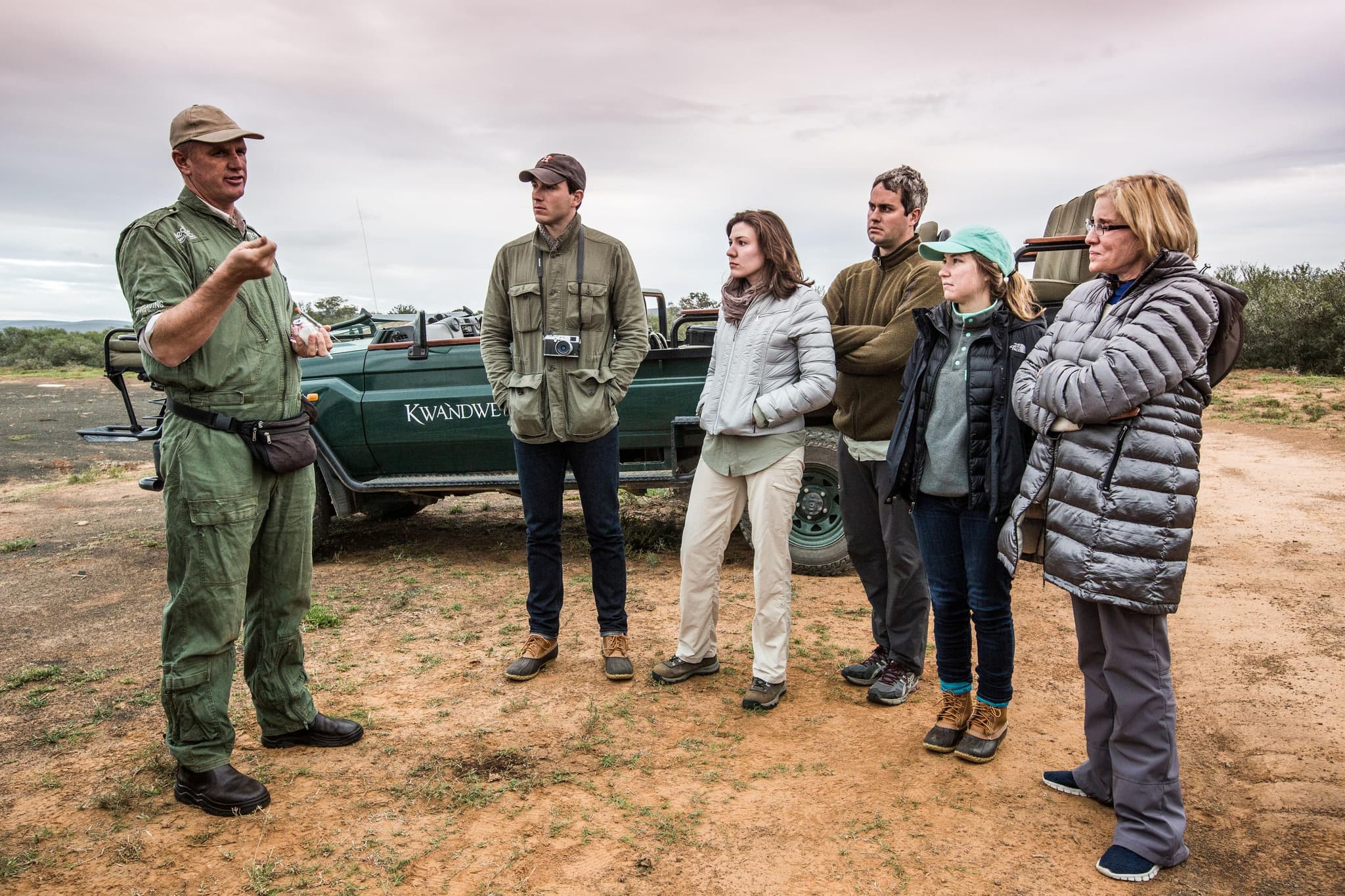 Conservation guide at Kwandwe explaining rhino protection efforts to a group of attentive visitors by a safari vehicle