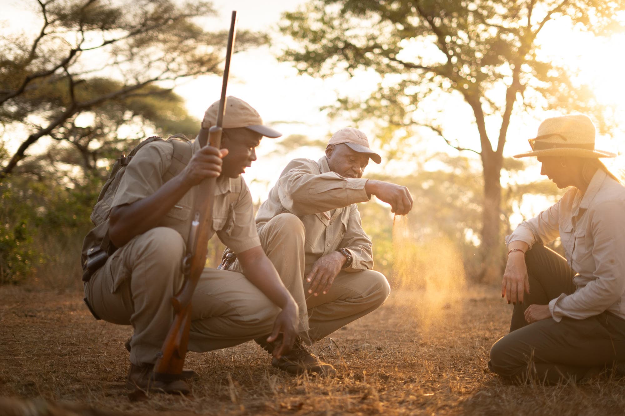 Safari guides teaching a guest to read animal tracks in golden sunset light