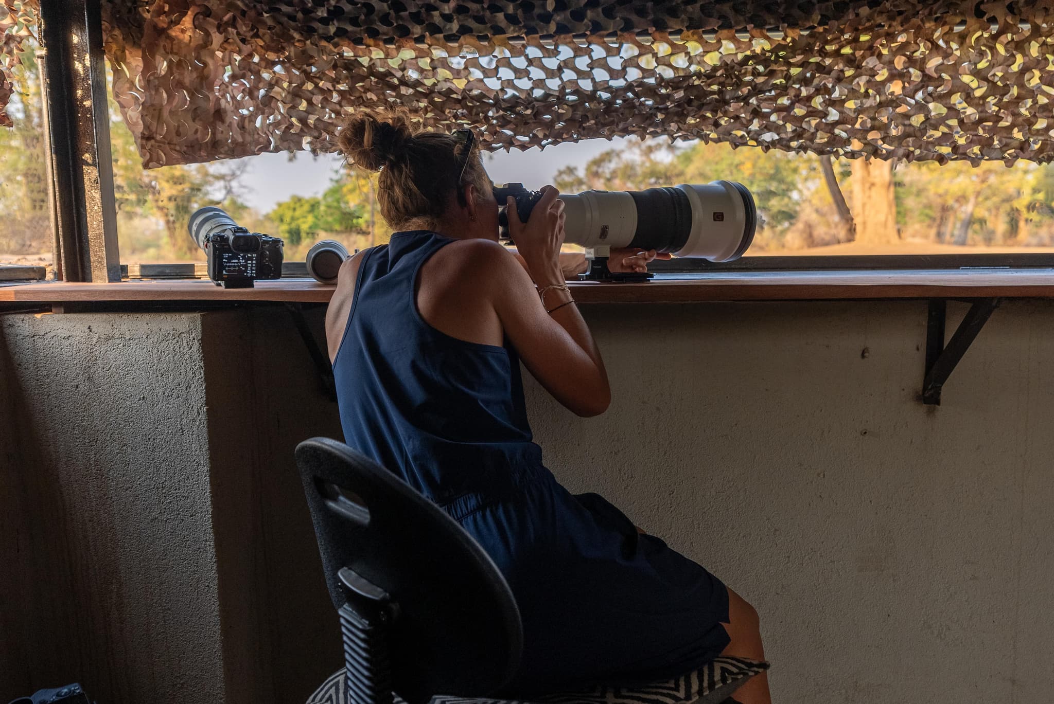 Woman photographing wildlife with a telephoto lens from a camouflaged hide