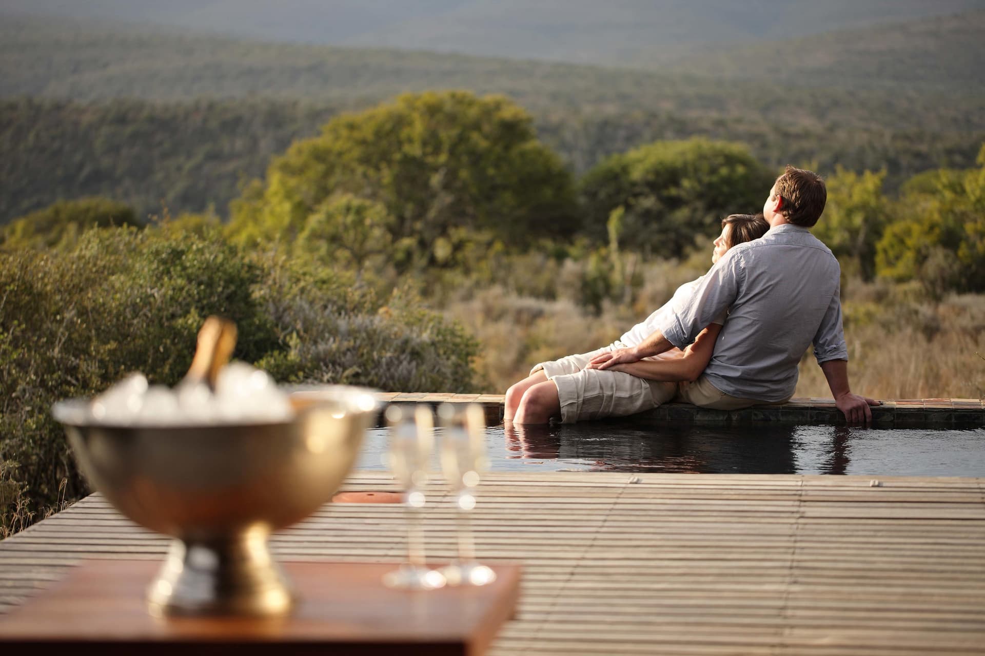 Couple relaxing by a private plunge pool with champagne overlooking the African bush