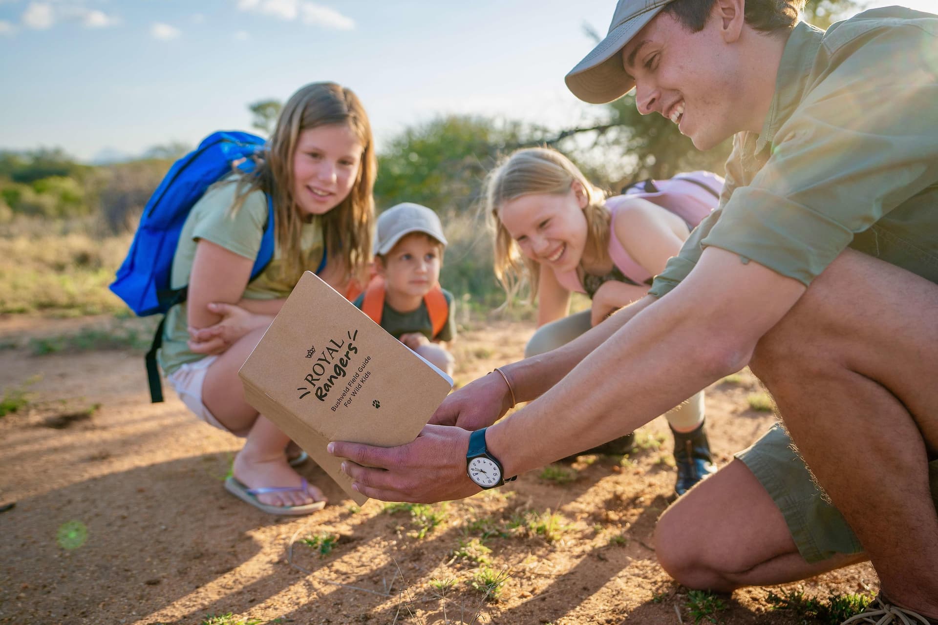 Safari guide showing children a Royal Rangers Bushveld Field Guide on a dusty trail